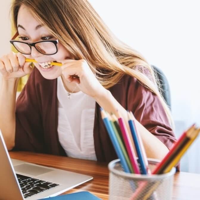 a woman biting a pencil while looking at a computer