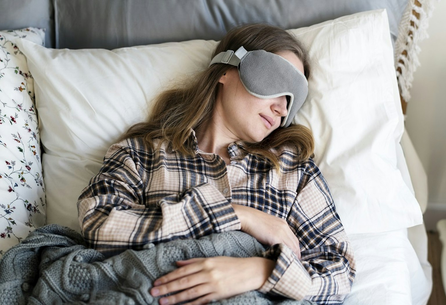 A woman, laying in bed, sleeping with a sleeping mask.