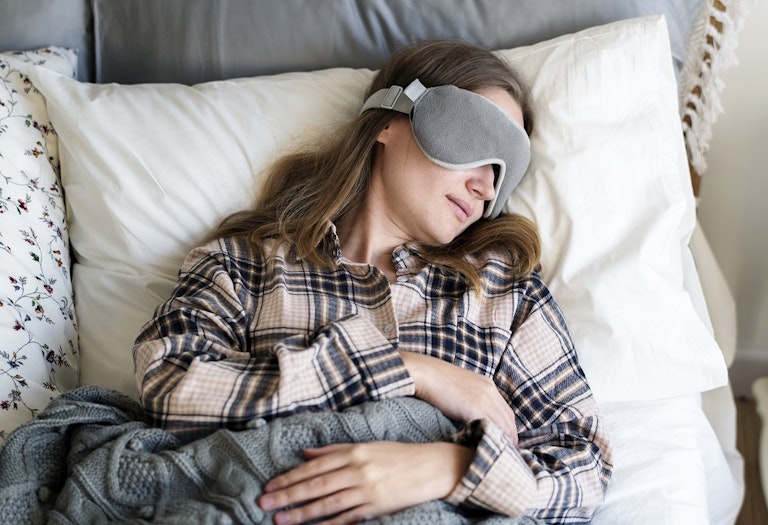 A woman, laying in bed, sleeping with a sleeping mask.